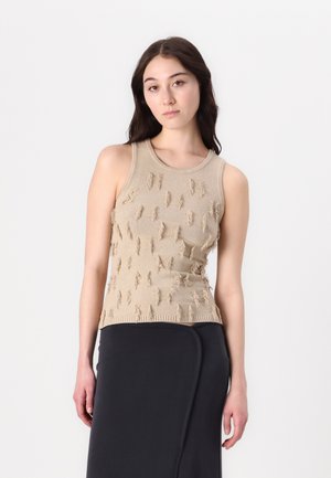 Beige strikket ermeløs topp med teksturert frynse detaljer, rund halslinje og tettsittende design, kombinert med en mørk skjørt.