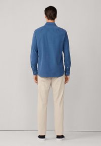 Camicia azzurra a maniche lunghe con colletto a camicia, abbinata a pantaloni chiari e scarpe da ginnastica scure. Tessuto morbido, vestibilità rilassata.