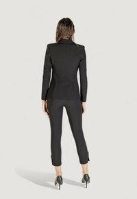 Černý tailoring blazer s formovanými rameny, doplněný úzkými kalhotami s rozparky na spodním lemu a lodičkami na vysokém podpatku. Hladký povrch tkaniny.