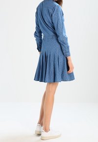 Denimklänning i ljusblått, med en åtsittande överdel, skjortkrage och veckad kjol. Designad med små kontrasterande prickar och knappar.