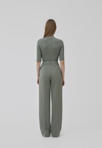 Grå ribbet bluse med 3/4 ærmer, parret med højtaljede, brede bukser i en matchende grå-grøn nuance. Glat tekstur, minimal detalje.