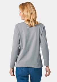 Hellgraues Langarmshirt mit rundem Ausschnitt, weichem Material, geradem Schnitt und minimalen Nähdetails, kombiniert mit blauen Jeans.