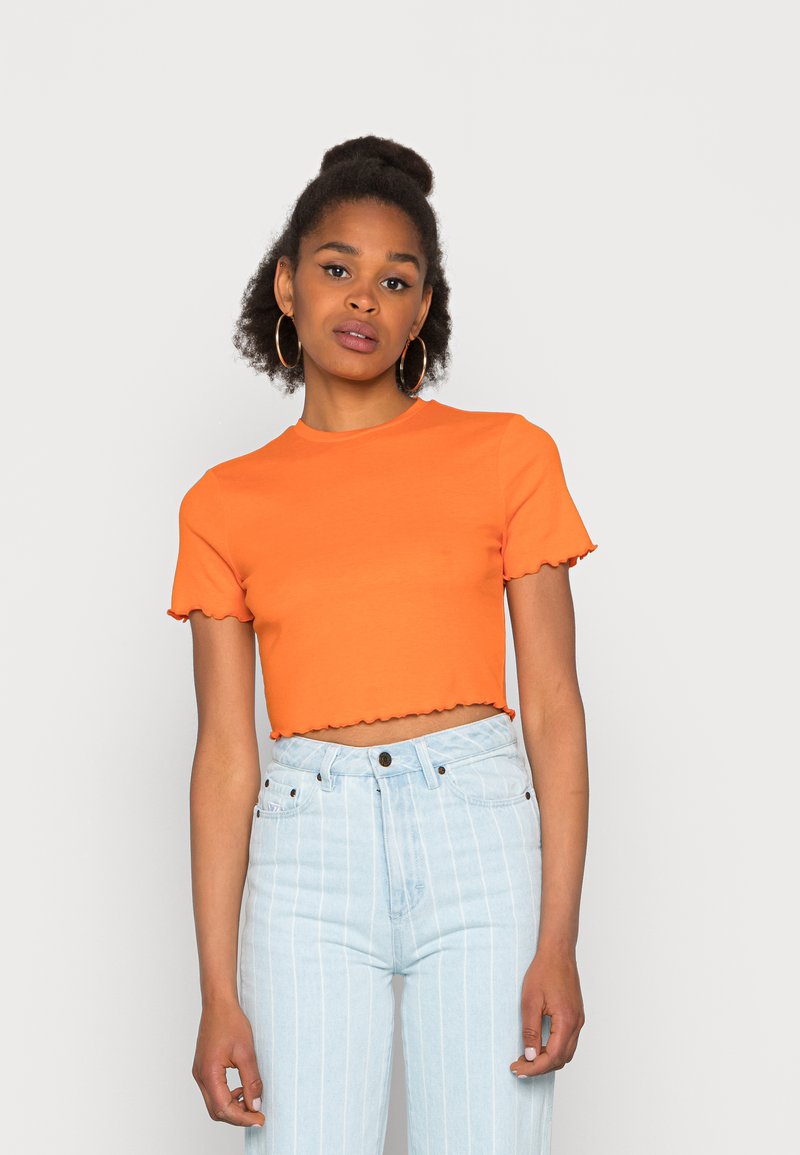 T-shirt curta laranja com mangas curtas e bainha em forma de escalope, combinada com jeans de cintura alta em azul claro com riscas verticais.