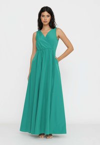 Abito lungo teal con design avvolgente, senza maniche e girovita arricciato. Realizzato in tessuto morbido, scende fino a terra con una silhouette fluida.