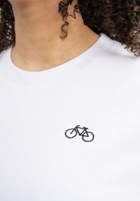 Weißes Baumwoll-T-Shirt mit einem kleinen schwarzen gestickten Fahrradesign auf der Brust, mit Rundhalsausschnitt und weicher Textur.