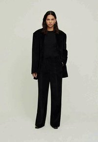 Black velvet suit with a structured blazer and wide-leg pants. The outfit features a ribbed black top underneath and minimalistic accessories.