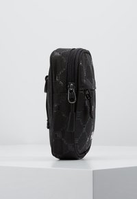 Czarna kieszonka zapinana na suwak z teksturowanej tkaniny, z delikatnym wzorem. Widok z boku podkreśla zaokrąglony kształt i podwójne suwaki.