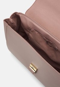 Intérieur d'un sac à main synthétique rose montrant un tissu doux, une poche et un fermoir doré texturé.
