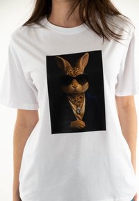Camiseta blanca con un gráfico de un conejo con gafas de sol y una cadena de oro, sobre un fondo negro.