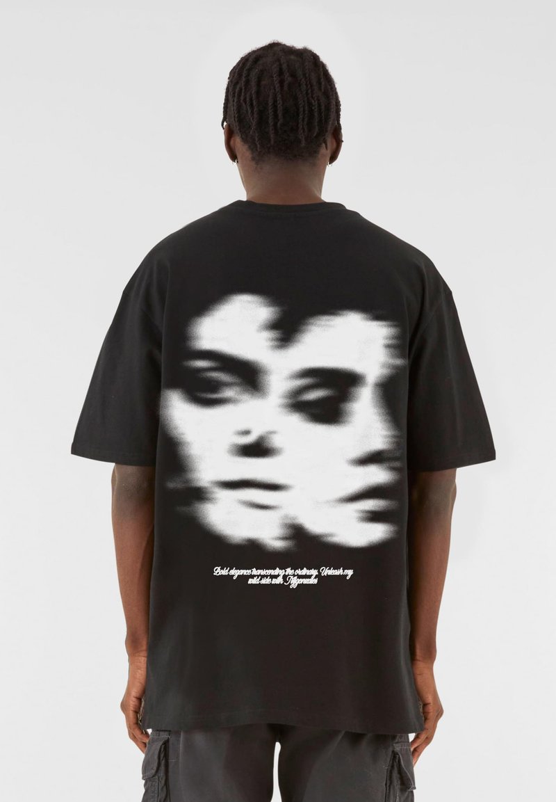 Svart bomulls-t-shirt med en suddig grafik av ansikten på baksidan, med vit text nedanför, korta ärmar och en avslappnad passform.