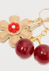 Nøglering med en beige læderblomst med en rød plastikblomsterkerne, guldfarvet hardware og røde glitrende kirsebærcharms.