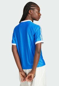 Jersey deportivo azul con rayas verticales, cuello blanco y tres rayas blancas en los hombros. El tejido parece suave y ligero.