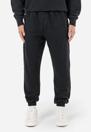 Joggers negros en tejido de mezcla de algodón, con cintura elástica, bolsillos laterales y puños acanalados. Diseño simple sin patrones visibles.