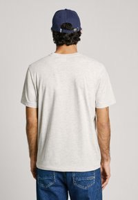 Light gray cotton t-shirt with short sleeves and a rounded neckline, worn with blue denim jeans and a dark blue cap.