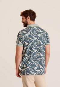 Korte mouwen polo shirt in crème met een groen en marineblauw bladerenpatroon. Heeft een contrasterende kraag met groene accentstrepen.