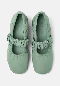 Gröna tygballettskor med ett samlat elastiskt band runt öppningen, med en mjuk, vadderad design och rund tåform.