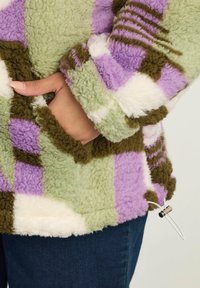 Fleece pullover met een patchworkontwerp in groen, lavendel, wit en bruin. Bevat een zak en een verstelbaar aantrekkoord aan de onderkant.