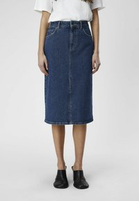 Jupe midi en denim bleu foncé, avec une coupe droite, une couture à l'avant et un design minimaliste. Portée avec des chaussures noires à enfiler.