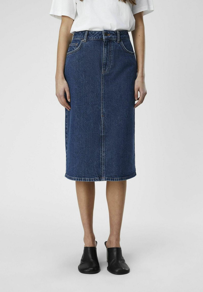 Falda midi de mezclilla en azul oscuro, con corte recto, costura delantera y diseño minimalista. Combinada con zapatos negros de tipo slip-on.
