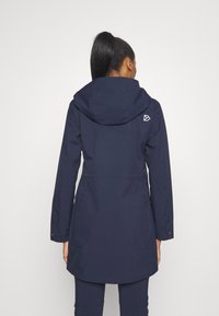 Marinblå vattentät jacka med huva, justerbara manschetter och en bakre ventil. Logodetalj på övre ryggen, slät textur.