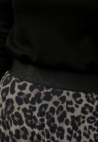 Černý elastický pás se vzorem s embosovaným textem "ENJOY" nad skládací sukní s leopardím potiskem v béžových a tmavě modrých tónech. Měkká textilie.