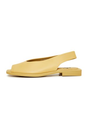 Scarpe slingback gialle con punta aperta, suola piatta, texture in pelle liscia e design minimalista. Accentate da un semplice ritaglio.