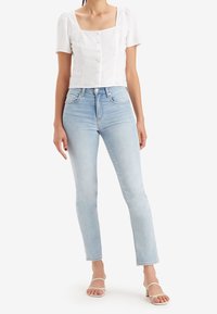 Camisa blanca corta con mangas cortas y escote cuadrado, combinada con unos vaqueros de tiro alto en azul claro y sandalias de tacón transparente.