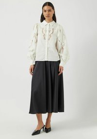 Hvit bluse med broderte detaljer og puffede ermer, kombinert med et langt svart satengskjørt og svarte spisse hæler.