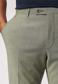 Jasnozielone spodnie o gładkiej fakturze, dopasowanym kroju, bocznych kieszeniach i pojedynczym zapięciu na guzik w pasie.