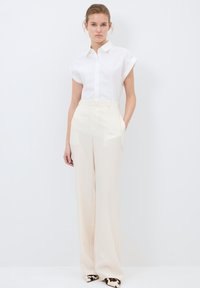 Chemise blanche à manches courtes et boutons, associée à un pantalon taille haute à rayures crème et des talons noirs et blancs à motifs.