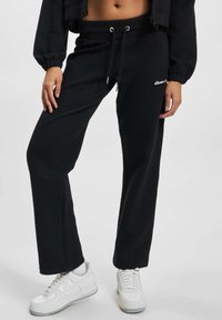 Czarne dresowe spodnie z prążkowanego materiału, z elastycznym pasem, sznurkiem i detalem z logo. W połączeniu z białymi trampkami.