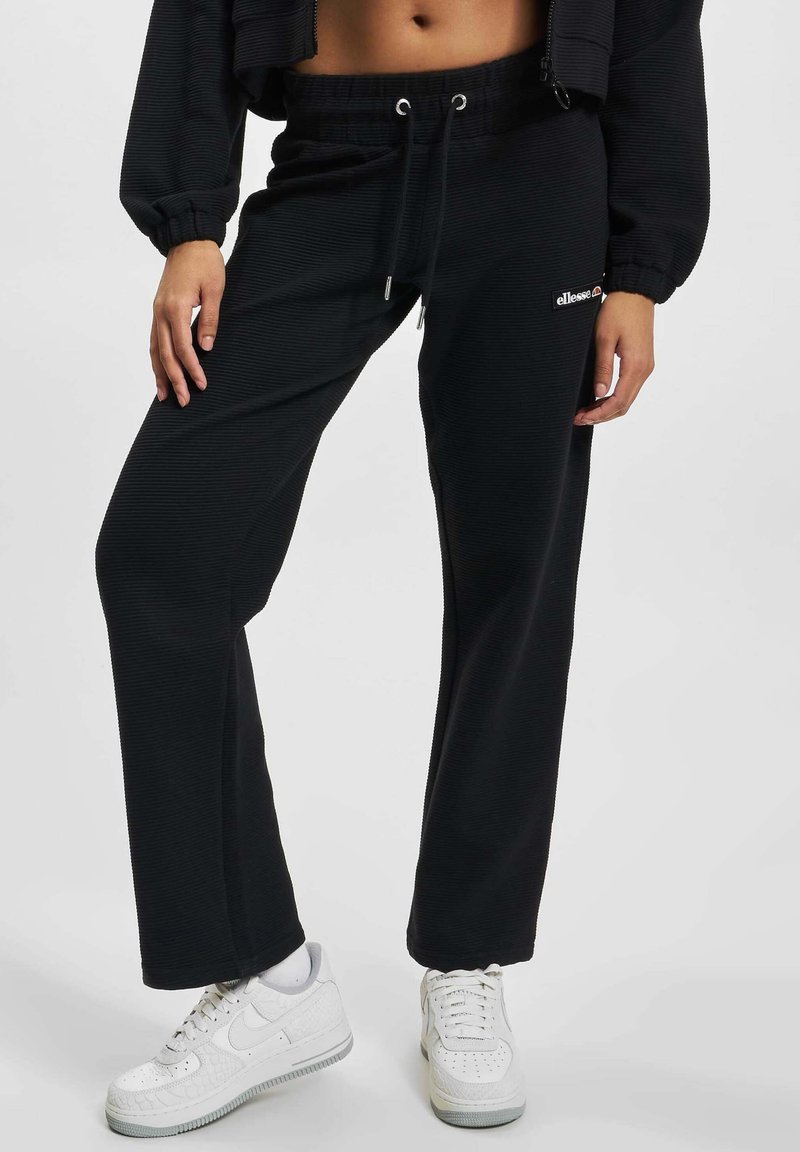 Czarne dresowe spodnie z prążkowanego materiału, z elastycznym pasem, sznurkiem i detalem z logo. W połączeniu z białymi trampkami.