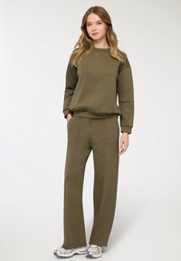 Felpa verde oliva e pantaloni a gamba larga abbinati realizzati in tessuto morbido, con scollo tondo e polsini a coste, abbinati a sneakers metalliche.