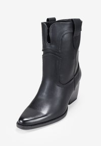 Botín de piel negra con punta afilada, detalles de costura, cortes laterales y un tacón bajo y ancho. Textura suave y diseño elegante.