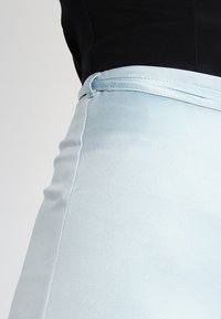 Light blue fitted pants with a smooth texture, featuring a sleek waistband and a minimalistic design. No visible hardware or patterns.