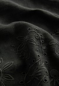 Svart broderad tyg med en slät textur, prydd med blommönster och små utskärningar som skapar en subtil kontrast i designen.