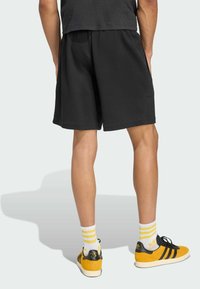 Pantaloni corti neri in felpa con una vita elasticizzata, texture morbida e tasche. Abbinati a sneaker gialle e nere e calzini bianchi a righe.