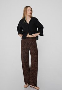 Černý zkrácený top s knoflíkovým zapínáním, kombinovaný s hnědými kalhotami se širokými nohavicemi s leopardím vzorem. Model má na sobě žabky, čímž předvádí ležérní outfity.