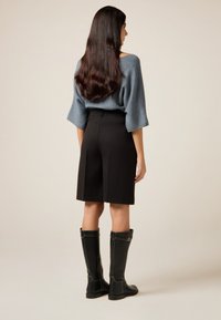 Blå oversized tröja med vida ärmar, svarta skräddarsydda shorts och knähöga svarta stövlar med sömmar och metallaccenter.