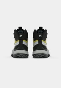 Botas de senderismo con un upper negro y amarillo, entresuela gris, suela de goma texturizada y un diseño de soporte para los tobillos con tiradores.