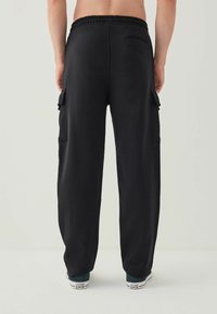 Sorte cargobukser med en afslappet pasform, elastisk talje, to sidelommer og ribbede cuffs. Bæres med mørke sneakers.