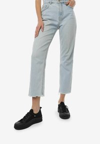 Lysblå højtaljede denimjeans med lige snit, rå kant og sidelommer, parret med sorte lærreds sneakers.