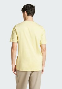 Žluté tričko s krátkým rukávem vyrobené z měkké bavlny, s kulatým výstřihem a volným střihem. Zadní pohled ukazuje hladkou texturu a jednoduchý design.