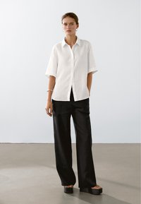 Wit linnen overhemd met korte mouwen, gecombineerd met zwarte, wijde broek met hoge taille en platformsandalen. Minimalistisch ontwerp.