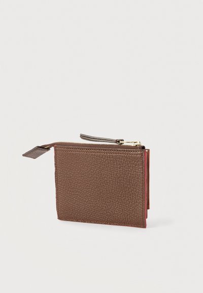 Καφέ πορτοφόλι από δερμάτινη υφή με φερμουάρ και ρίγα τράβηγμα σε απλό ανοιχτόχρωμο φόντο, παρουσιάζεται ελαφρώς από πλάγια γωνία.