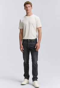 Maglietta bianca a girocollo, jeans in denim scuro e scarpe da ginnastica bianche. Vestibilità slim, dettagli minimalisti e texture uniforme in tutto l'outfit.