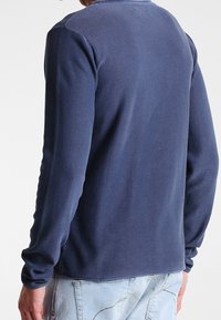 Granatowy sweter z długim rękawem o zaokrąglonym dekolcie i dopasowanych mankietach, charakteryzujący się gładką teksturą i luźniejszym krojem z tyłu.