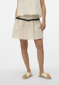 Beige cotton top with black print, layered over a matching skirt featuring a black lace waistband, paired with yellow slide sandals.
