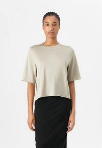 Short-sleeve, cropped T-shirt in light beige fabric with a smooth texture. Rounded neckline and minimalistic design paired with a black skirt.
