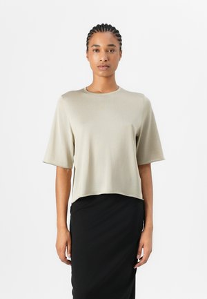 Kurze Ärmel, verkürztes T-Shirt aus leicht beige Stoff mit glatter Textur. Runder Ausschnitt und minimalistisches Design kombiniert mit einem schwarzen Rock.